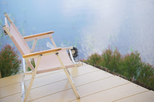 empty foldable beach chair on wooden deck overlooking calm water lake with copy space
