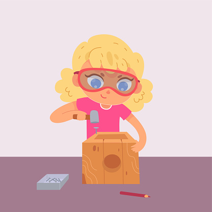 Cute kid making wood birdhouse, funny school girl in goggles woodworking with mallet