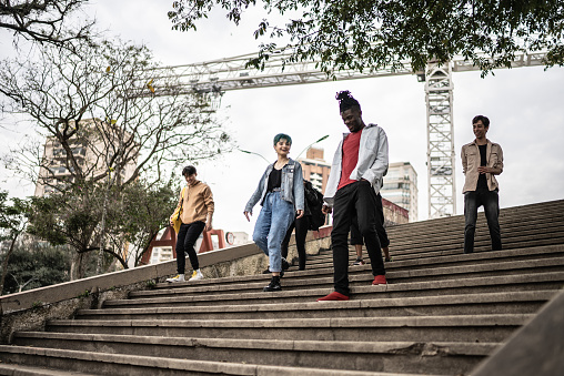 Rear view of business people moving up stairs. Male and female professionals walking on sunny day. Full length of colleagues are in long coat and suit.