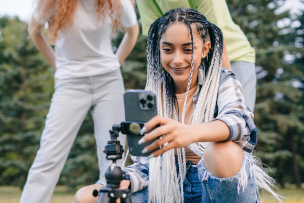 istock Woman using video sharing app on mobile phone while standing outdoors in the park with her friends. Modern communication, social media and gadgets. 1422660668