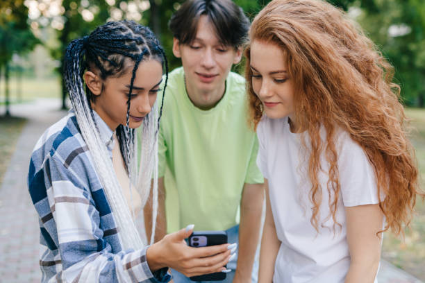 istock Three young friends standing outdoors in the park watching a interesting streaming video online. Friendship fun concept with trend technology interaction. Technology digital gadget. 1422662484