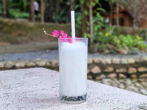 White milk in a glass is placed on the table. Additional decoration with small pink flowers, blurred background, focus on glass.