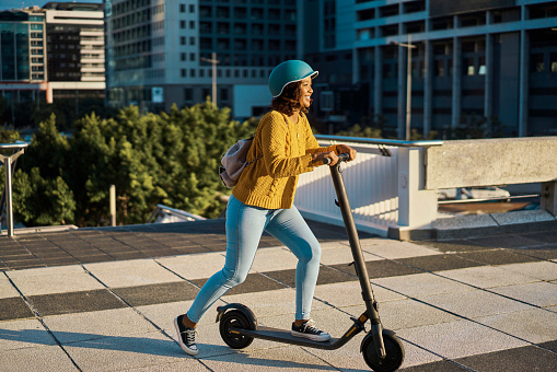 Electric scooter travel in the city with a happy woman from Mexico riding in a urban town. Female Mexican traveler with a smile using eco friendly, sustainability and green energy transportation