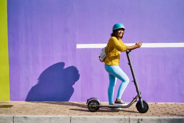 Woman, electric scooter and city travel for fashion student by building background with social media phone. Happy, cool model on eco friendly, environment carbon footprint and future energy transport