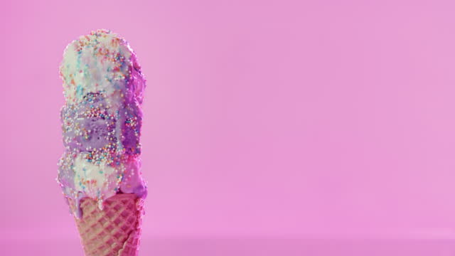 Ice cream melting, hot summer and candy sprinkles, with a pink mock up background. Blueberry and vanilla ice cream cone, dripping in heat. Happy holiday fun and a sweet dessert on a waffle cone.