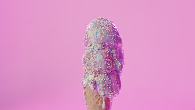 Closeup of a dripping and melting ice cream cone with colorful sprinkles in studio with copy space. Purple, frozen and cold summer dessert falling with a pink background and copyspace.