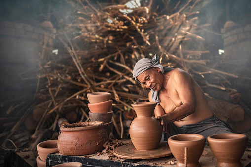 A senior man is using a potter's wheel to make pottery from wet clay.