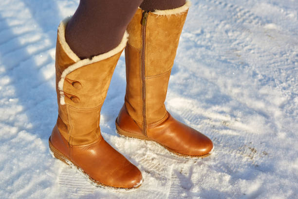 Leg woman winter brown fur boots walking on the snow in a winter park. Closeup outsole of warm boot. stock photo