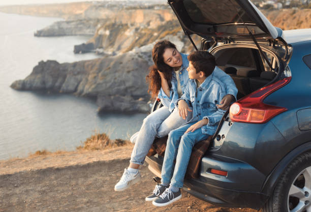 Family trip to the mountains by car. Mom is having fun with her teenage son, sitting in the trunk of a car and enjoying the view together Family trip to the mountains by car. Mom is having fun with her teenage son, sitting in the trunk of a car and enjoying the view together. car trunk stock pictures, royalty-free photos & images