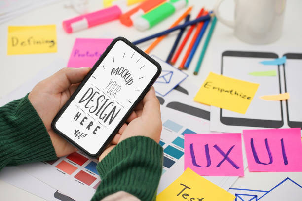 istock Creative UX UI designer hand holding mobile white screen mockup at working desk space. White screen for graphic montage. 1422702409