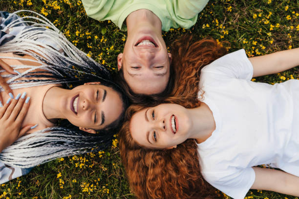istock Young three hipster adolescents lying down on the green grass, enjoying a sunset relaxation in a park, looking up at camera and smiling. Happy teenager portrait. Summer outdoor fun activity. Top view. 1422704541