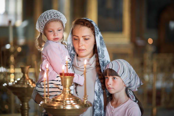 Young mother and her little blond Caucasian daughter with candles in Orthodox Russian Church stock photo