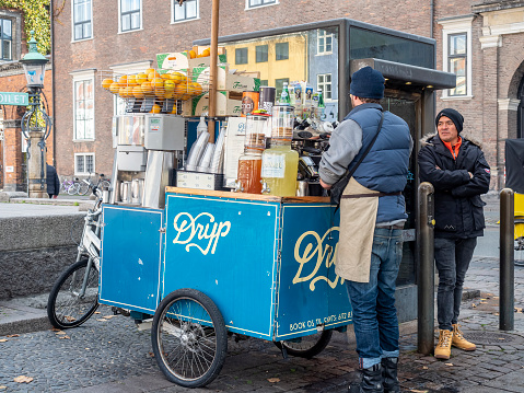 Copenhagen, Denmark - Oct 19, 2018: Dryp three-wheel miniature mobile cafe stall at the Nyhavn area. Owner sells fresh fruit juices and hot coffee. A customer beside having a chat.