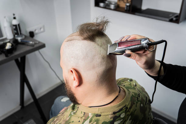 un jeune homme en uniforme militaire se rase la tête chauve pour le service militaire. un gars avec une barbe se fait couper les cheveux dans un salon de coiffure. - employee barracks photos et images de collection