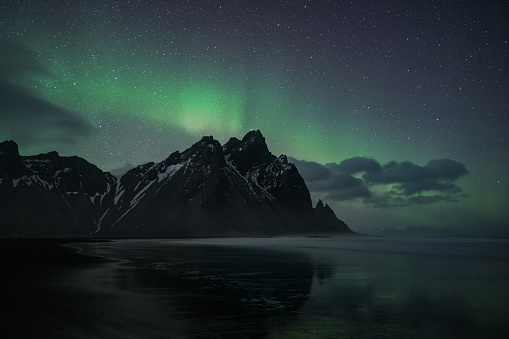 Volcanic Black Beach at Vestrahorn Mountain with unedited natural polar lights - northern lights aurora in wintertime. Moody Sky ,Black Beach, Sea and famous Mountain Range. Aurora Night Skyscape. Vestrahorn Mountain Range, Stokkness, South East Iceland, Nordic Countries, Northern Europe.