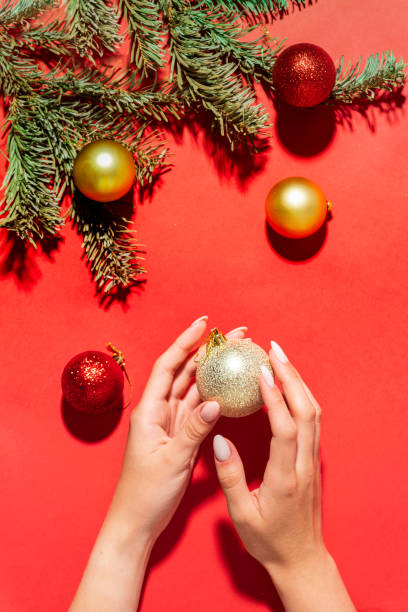 クリスマスツリーの枝とボール、冬のハンドケアと赤い背景に美しい女性の手。クリスマスの新年のテーマ。 - christmas fashion model human arm beautiful ストックフォトと画像