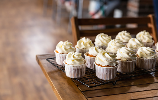 Beautiful vanilla cupcakes with cream cheese frosting on metal grille. Delicious homemade dessert. Blurred background.