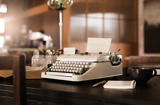 Old typewrite with coffee cup and book on wooden desk in old office room, retro style, vintage color tone