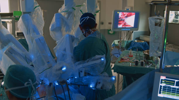 nurse looks at a monitor and medical devices while a surgeon performs an operation. - robotchirurgie stockfoto's en -beelden