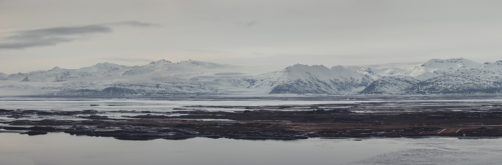 Southeast Iceland Lónsvík Snowcapped Mountain Range in Winter. XXXL Stiched Canon R5 Panorama of snowcapped Mountain Range close to Stokkness under overcast moody sky in winter twilight. Seawater fjord - lake in the panorama foreground. Southeast Iceland Lónsvík -Vesturhorn, Iceland, Northern Europe.