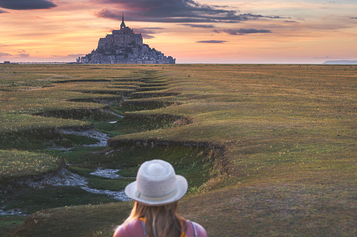 Young girl enjoying the View of the St Michael's Mount during beautiful sunset, Mont Saint Michael, France.