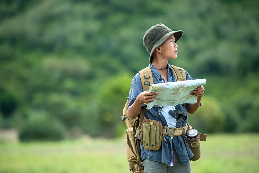 Asian boy backpack checking map and pointing in jungle forest, trips adventure and tourism for destination leisure for education and relax in nature park .  Travel vacations Concept