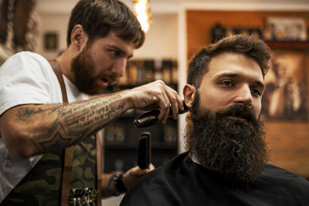 istock Young barber making haircut to a bearded man using electric razor 1422731950