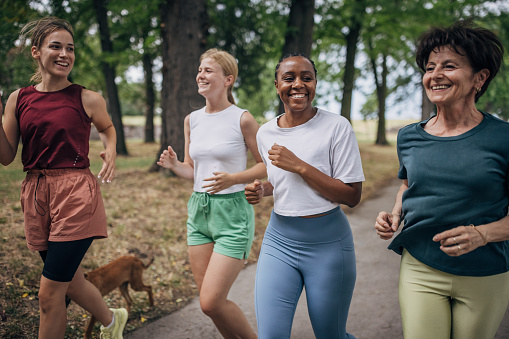Diverse group of women jogging together on a summer day in public park.