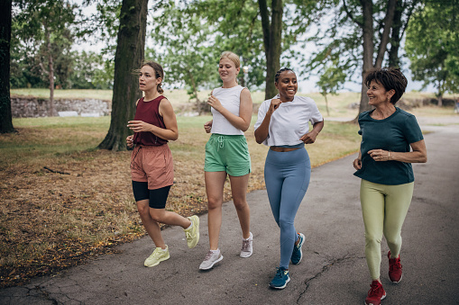 Diverse group of women jogging together on a summer day in public park.