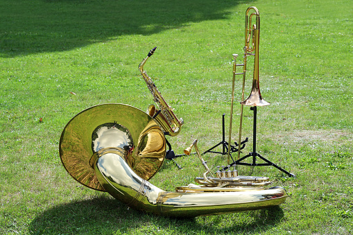 Various musical brass instruments like sousaphone, trombone and saxophone placed on the lawn in the park and waiting to be used in the music band, copy space