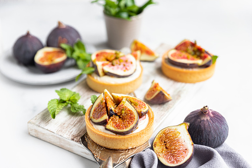 Tartlets with delicate cream cheese and fresh figs decorated with mint and pistachio, gray background. Autumn dessert. National Dessert Day, October 14.