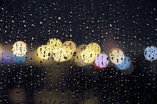 Texture of raindrops on window glass with defocused lights on the background