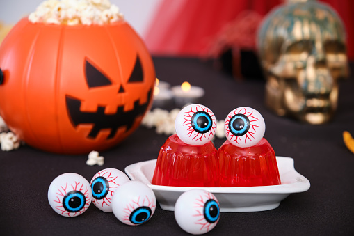Halloween snacks table with eyeballs on red jelly and pumpkin with popcorn. Sweets for Halloween party.