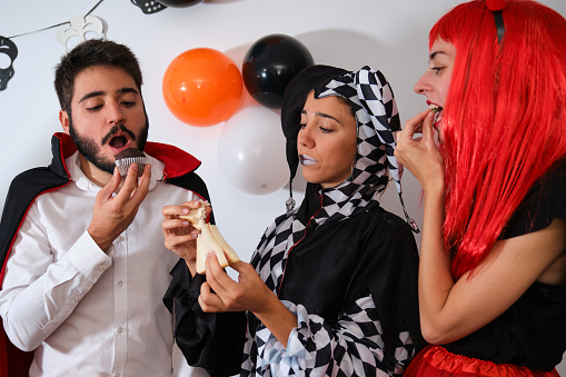 Three people eating at a costume Halloween party in a house.