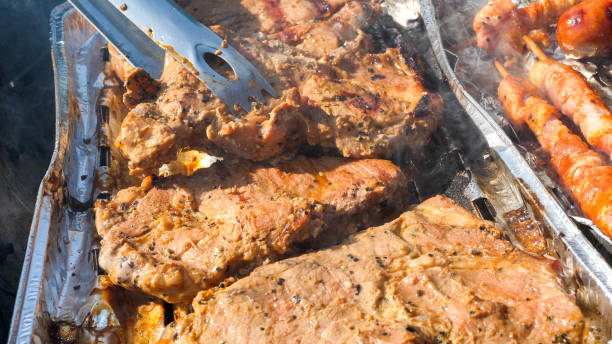 Close up of meat on a aluminum tray cooking on the grill