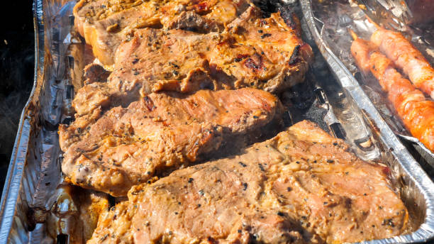 Close up of meat on a aluminum tray cooking on the grill