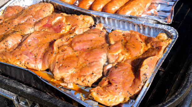 Close up of raw meat on a aluminum tray cooking on the grill