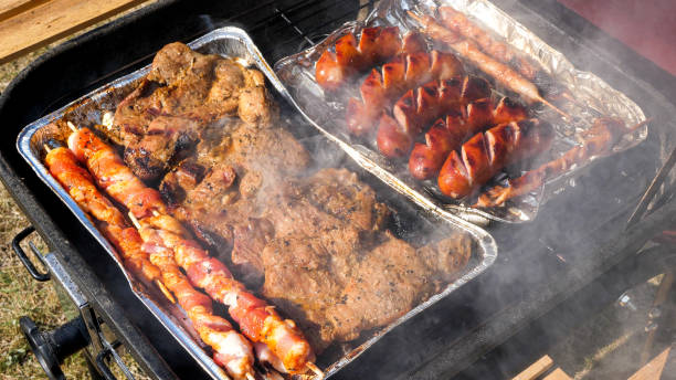 Close up view of sausages and meat grilling on an aluminum tray