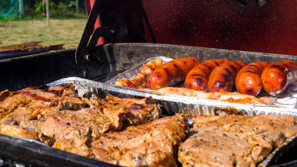 Close up view of sausages and meat grilling on an aluminum tray