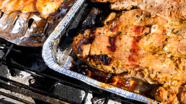 Close up view of sausages and meat grilling on an aluminum tray