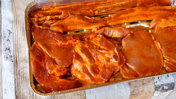 Raw meat laying on an aluminum tray prepared for grilling