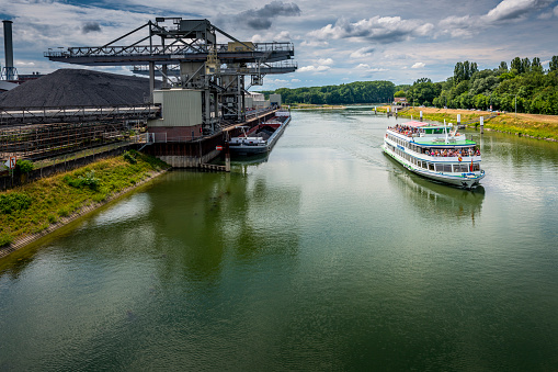 Karlsruhe, Germany - June 26, 2022: Tourboat Karlsruhe full with sightseeing tourists beside a coal-fired power station.