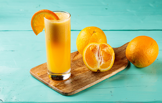 Fresh Orange Juice with raw oranges served in a glass isolated on cutting board side view healthy fruit juice