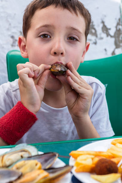 Young boy in a mustard yellow shirt enjoying a sweet dessert at an outdoor cafe. Relaxed family atmosphere.