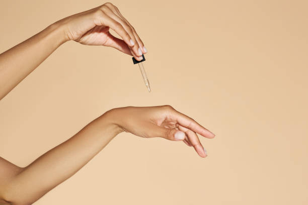 Moisturizing skin of hands with essential oil or serum. Woman applying essential oil to her hands with pipette dropper on beige background Moisturizing skin of hands with essential oil or serum. Woman applying essential oil to her hands with pipette dropper on beige background serum sample stock pictures, royalty-free photos & images