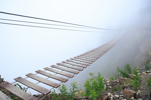 Hanging rope bridge vanishing in fog. Tourist suspension bridge.