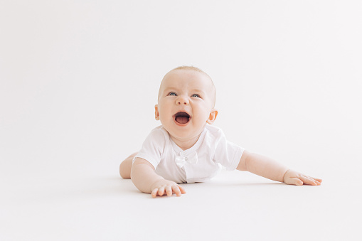 Happy baby boy laughs cheerfully lying against white background.