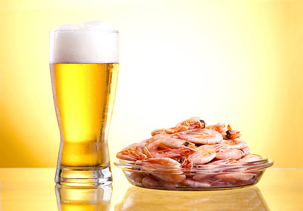 One glass of beer and cooked shrimp on a plate One glass of beer and cooked shrimp on a plate on a yellow background food state preparation shrimp prepared shrimp stock pictures, royalty-free photos & images