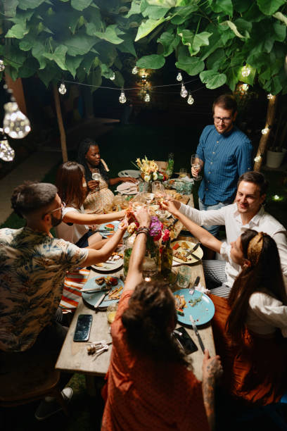 Multi-ethnic friends toasting drinks at dinner table in yard Friends and family having lovely garden dinner party in the summer, autumn gay dinner table stock pictures, royalty-free photos & images