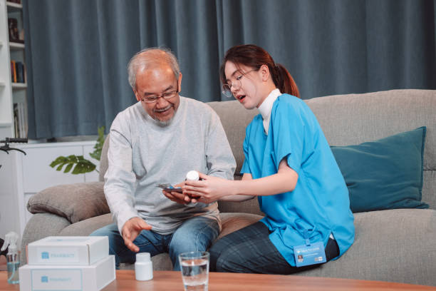 Asian senior male patient consult prescription drug with physician nurse at nursing home. Caregiver therapist pharmacist woman hold medicine pills bottle, medicine dosage at house in living room. paciente masculino mayor asiático consulta medicamentos recetados con enfermera médica en un hogar de ancianos. terapeuta cuidador farmacéutico mujer sostener píldoras de medicamentos botella, dosis de medicamentos en casa en la sala de estar.